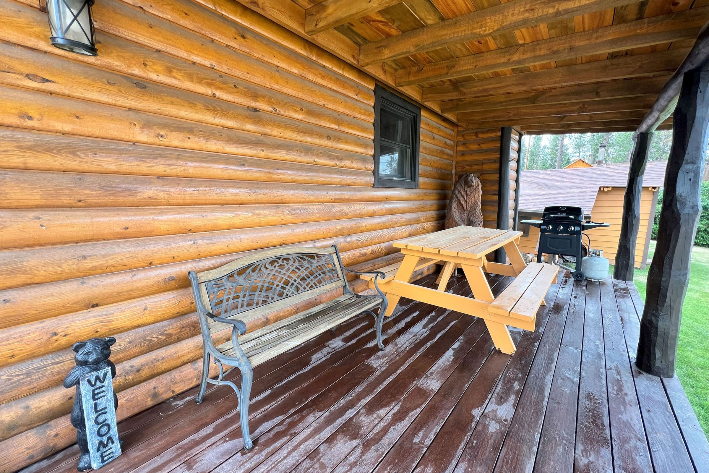 A bench and picnic table on the porch of a log cabin.