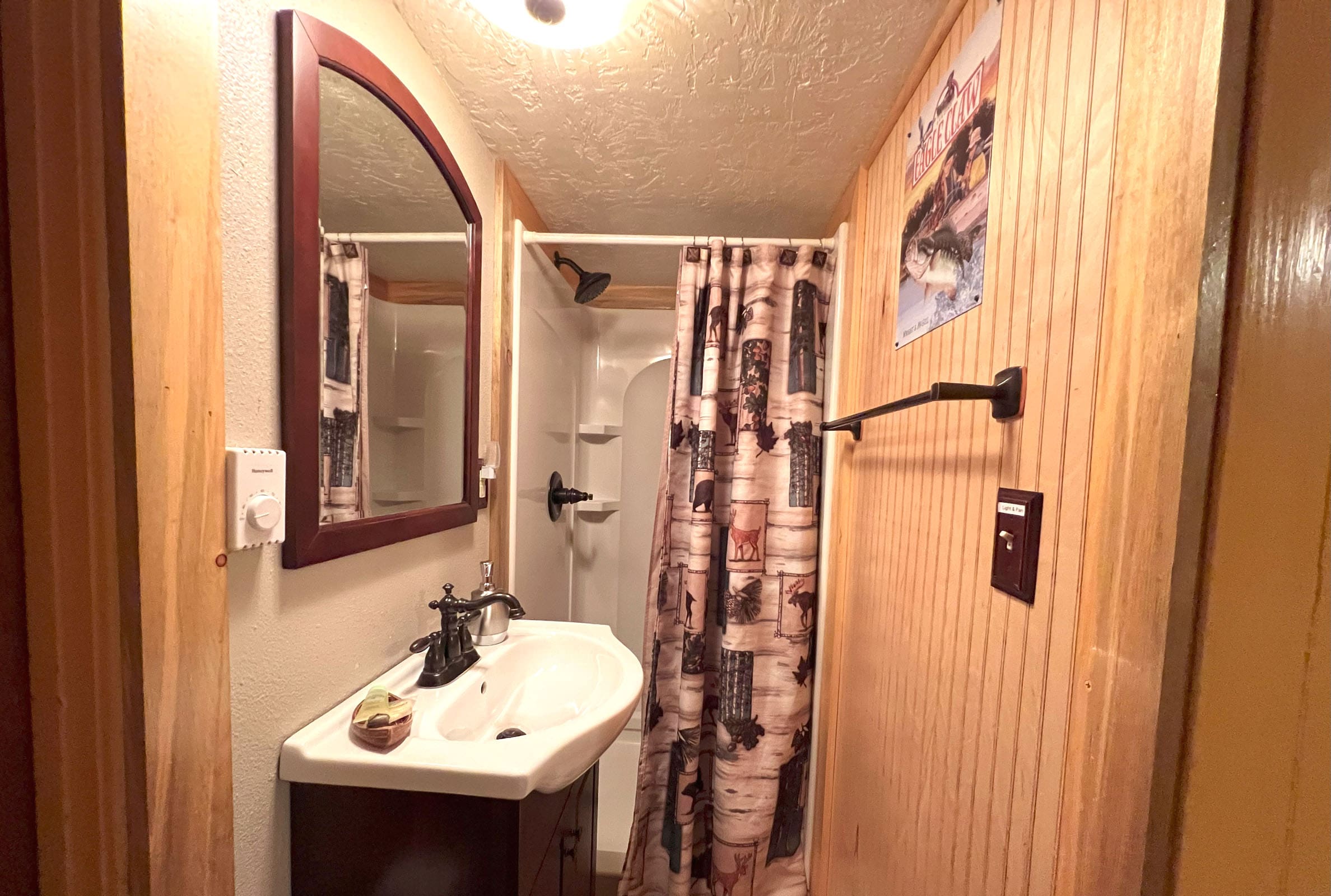 A bathroom with a sink, mirror and shower.