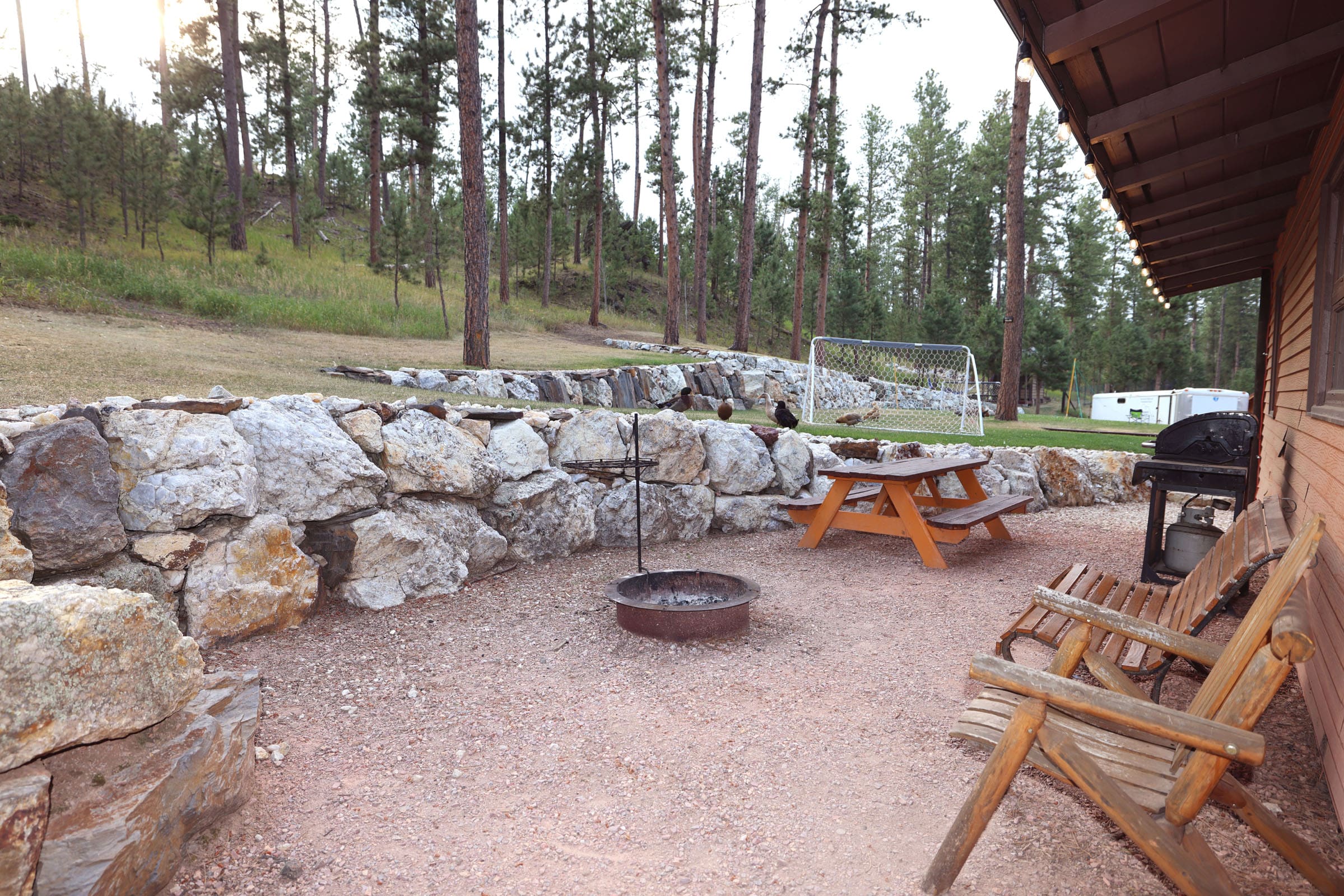 A picnic table and fire pit in the middle of a forest.